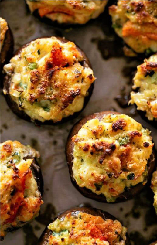 Close-up of several stuffed mushrooms topped with a golden-brown, crispy mixture of cheese, herbs, and breadcrumbs on a baking sheet. Discover how to make crab stuffed mushrooms that will elevate your appetizer game.